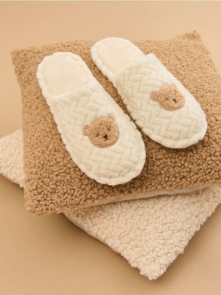 Strukturalne kapcie - kremowy. Białe obuwie domowe Sinsay, bez wzorów, bez zapięcia. Za 29.99 zł.